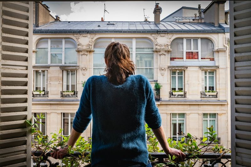 Vue depuis un apaprtement français avec une jeune femme se tenant au balconappartement français donnant sur une rue. Photo by Aurélien Lemasson-Théobald on Unsplash